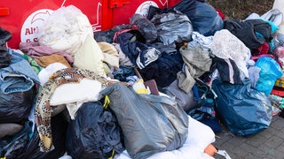 Ein Berg alter Klamotten vor einem Altkleidercontainer