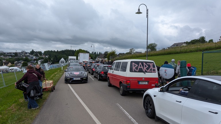 Fahrzeuge stehen in Schlange, die Fans für Rock am Ring laufen entlang der Straßen von Nürburg.