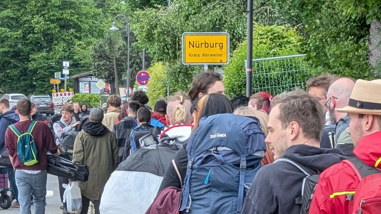 Mit Gepäck, Pavillons und Campingausrüstung warten die ersten Fans auf die Eröffnung der Campingplätze fürs Festivalwochenende.
