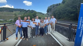 Am Ortsausgang Marienthal: Mehrere Politiker stehen auf einer neu errichteten Fahrradbrücke über der Ahr. Sie haben symbolisch ein Band zerschnitten als Zeichen der Wiedereröffnung.