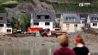 Zwei junge Menschen stehen im Mayschoss am Ahrufer und schauen auf die Zerstörung durch das verheerende Hochwasser im Ahrtal.