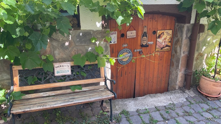 Weinlaub rankt um eine Tür in einer Bruchsteinmauer, davor steht eine Sitzbank: Idyllische Szene aus dem Moselort Bremm, der laut dem Magazin GEO zu den schönsten Dörfern Deutschlands zählt. 