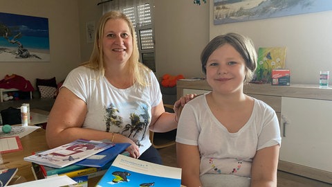 Kirstin Marx und ihre Tochter Emilia sitzen am Tisch auf dem die Schulbücher für das neue Schuljahr liegen.