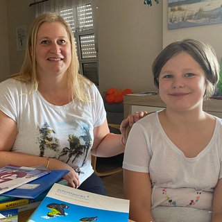 Kirstin Marx und ihre Tochter Emilia sitzen am Tisch auf dem die Schulbücher für das neue Schuljahr liegen.