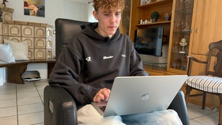 Tom Groß sitzt auf einem Sessel an seinem Laptop.