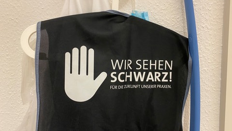 Eine Weste in einer Landauer Hausarztpraxis mit der Aufschrift: "Wir sehen schwarz für die Zukunft unserer Praxen."
