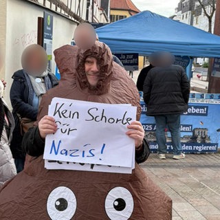 Mann protestiert in Neustadt in einem Kostüm, das wie ein Kackhaufen aussieht