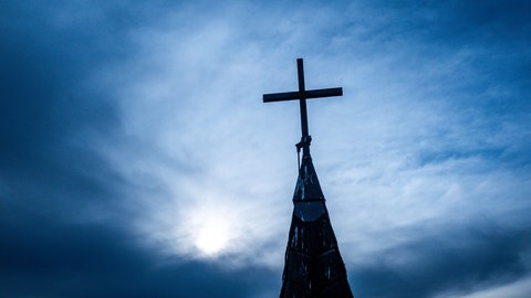 Kirchenkreuz auf dem Dach einer entwidmeten Kirche, Symbolbild für: Wenn die Kirche zur Kita oder Arztpraxis wird
