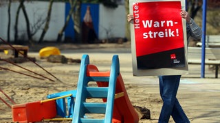 Mann hängt Bild in Kita auf für Warnstreik, Symbolbild für Streiks in der Pfalz
