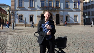 Bürgermeister Hartmann mit seinem Baby auf dem Arm auf dem Weg ins Rathaus Landau - er bekommt keine Elternzeit.