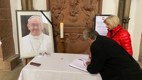 Ein Ehepaar schreibt ins Kondolenzbuch zum Tod von Papst Franziskus im Speyerer Dom