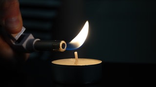 Eine Frau zündet mit einem Feuerzeug ein Teelicht an (Illustration). In Böhl-Iggelheim, Deidesheim, Ludwigshafen-Oggersheim und Ludwigshafen-Friesenheim ist es am Sonntag zu Stromausfällen gekommen.