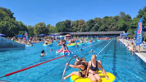 Kinder und Erwachsene spielen und schimmen in einem Freibadbecken.