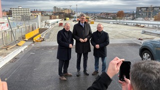 Bundesverkehrsminister Patrick Schnieder steht mit Vertretern aus Ludwigshafen auf der Baustelle einer Hochstraße.