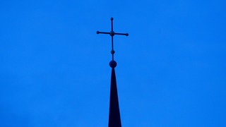 Das Kreuz einer evangelisch-lutherischen Kirche ist in der Abenddämmerung zu sehen (Symbolbild). Am zweiten Tag ihrer Herbsttagung hat die Landessynode der Evangelischen Kirche der Pfalz in Speyer einem Gesetzentwurf zur Änderung der Kirchenverfassung zugestimmt.