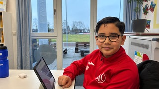 Ein Schüler sitzt im Fußball-Dress am Computer. Beim Ludwigshafener Fußballverein LSC heißt es für die Kinder: Erst Hausaufgabenbetreuung, dann Sport.