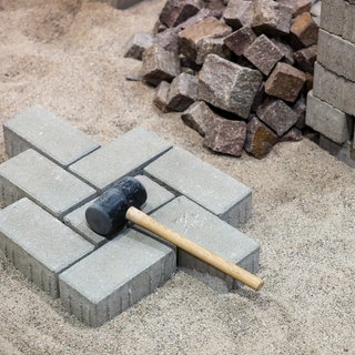 Hammer auf einem teilweise fertiggestellten Pflaster - Symbol für Handwerk beklagt steigende Kosten durch Staus auf der Rheinbrücke 