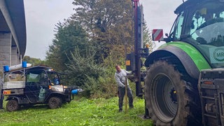Zwei Männer errichten am Rande eines Ackers einen Zaun. In Rheinhessen werden weitere Zäune aufgestellt, um die afrikanische Scweinepest einzudämmen. 
