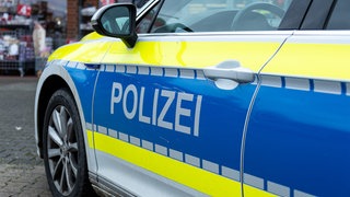 Im Vordergrund die Fahrertür eines Polizeiautos mit dem großen Schriftzug "Polizei", im Hintergrund ein Geschäft. (Sujetbild)