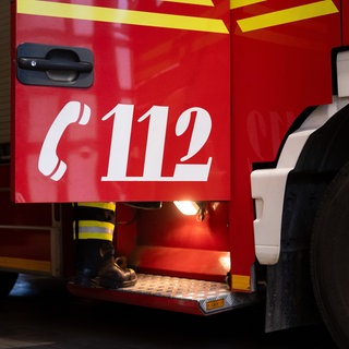Ein Feuerwehrmann steigt in ein Einsatzfahrzeug - auf der geöffneten Tür steht die Nummer "112".