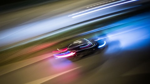 Ein Auto fährt sehr schnell auf einer Straße, die Scheinwerfer sind zu Lichtspuren verwischt.