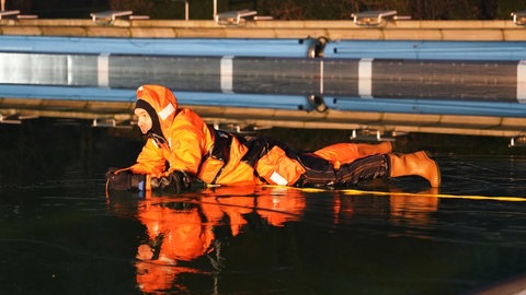 Ein Feuerwehrmann liegt auf der gefrorenen Wasseroberfläche eines Beckens im Alzeyer Wartbergbad.
