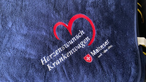 Eine dunkelbaue flauschige Decke mit Herzenswunsch-Logo und Malteser Logo für die Patienten.