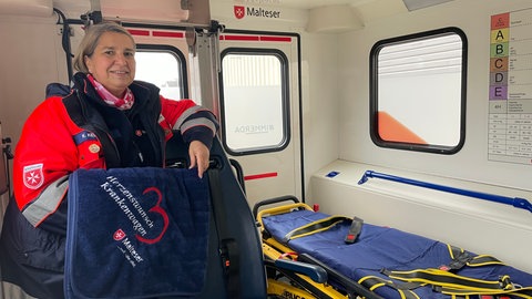Katja Kessel steht mit der blauen Flauschdecke in der Hand im Herzenswunsch-Mobil der Malteser.