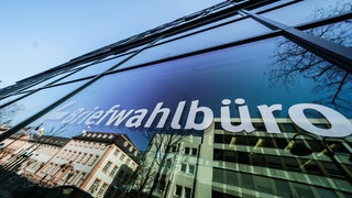 Auf der sich spiegelnden Glasfront des Stadthauses Große Bleiche in Mainz steht "Briefwahlbüro".