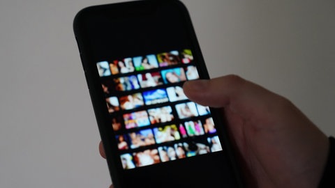 Ein Mann schaut sich auf einem Smartphone eine Porno-Internetseite an. Die Bilder sind unscharf. Das Foto ist ein Symbolbild. 