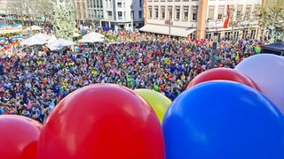 Am Balkon des Ostheimer Hofes sind bierfarbbunte Ballonsbefestigt. Unten feiern die Fastnachter. 