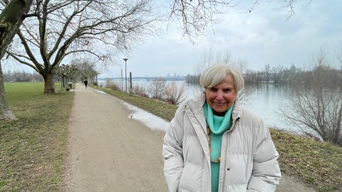 Rosi steht am Rheinufer, im Hintergrund die Silhouette von Mainz