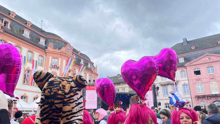 Frauen haben sich pinkfarbene Perücken aufgesetzt und haben pinkfarbene, herzförmige Luftballons dabei.