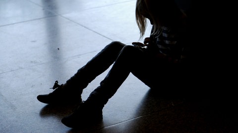 Ein kleines Mädchen sitzt mit gesenktem Kopf allein auf dem Fußboden. Wegen Corona haben viele Kinder psychische Probleme.