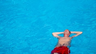 Ein Mann treibt auf dem Rücken in einem Freibad und genißet die Sonne.