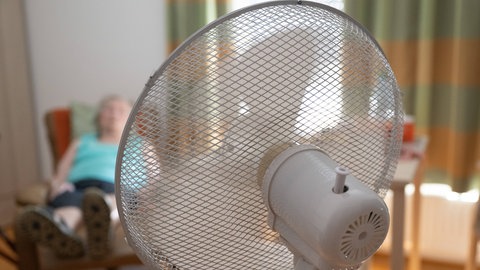 Seniorin liegt auf Sessel und kühlt sich mit Ventilator ab