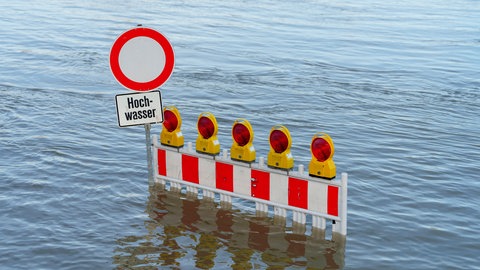 Eine Straßenabsperrung ist vom Hochwasser des Rheins überflutet.