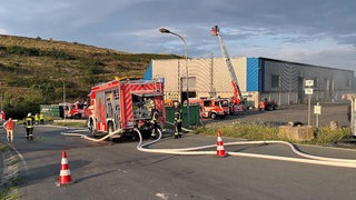 Feuerwehrautos stehen vor der Lagerhalle auf der Mülldeponie in Wiesbaden, in der es gebrannt hat. 