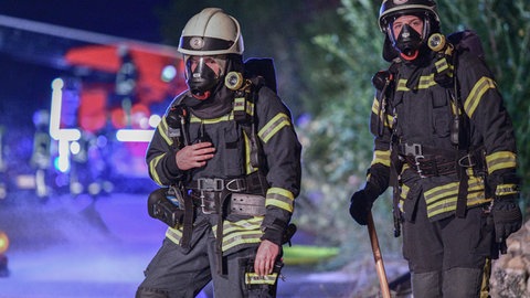 Feuerwehrleute stehen im Dunklen vor einem Löschwagen (Symbol). Feuerwehrleute (Symbol). Bei der Berufsfeuerwehr Mainz ist es nun möglich eine Ausbildung zu machen ohne vorher eine Berufsausbildung abgeschlossen zu haben. 