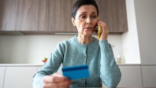 Eine Frau telefoniert und hält dabei eine Bankkarte in der Hand. In Mainz haben falsche Bankmitarbeiter mit einer neuen Betrugsmasche mehrere tausend Euro erbeutet