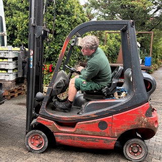 Obstbauer sitzt im Gabelstapler und verlädt Obstpaletten in einen Transporter