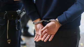 Ein Polizist führt einen Verdächtigen Mann mit Handschellen ab. (Symbolbild)