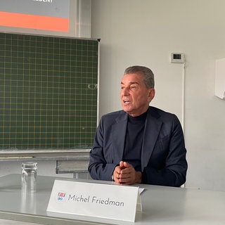 Michel Friedman sitzt an einem Pult. Der Publizist hat das Otto-Schott-Gymnasium im Rahmen des ARD-Jugendmedientags besucht. 