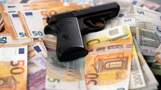 Ein Pistole auf geraubten Banknoten liegend. (Symbolfoto)