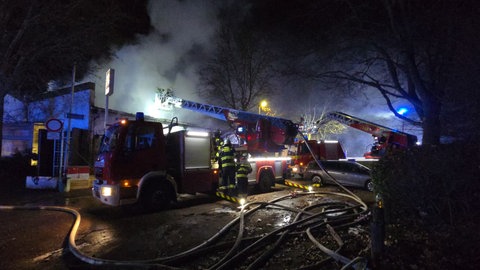 Einsatzkräfte und Feuerwehrautos stehen vor dem völlig verqualmten Reitstall in Mainz-Hechtsheim.