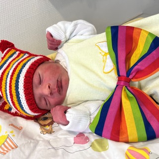 Ein neugeborener Säugling mit vierfarbbunter Mütze. Der Junge kam im Marienhaus Klinikum Mainz zur Welt und ist das erste Rosenmontagsbaby 2026 