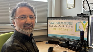 Mustafa Cimşit, Geschäftsführer von Maimonids, sitzt an seinem Schreibtisch vor seinem Computer.