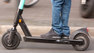Männerbeine auf einem E-Scooter: In Mainz hat sich ein Mann, der mit einem Haftbefehl gesucht wurde, eine Verfolgungsjagd mit der Polizei geliefert. 