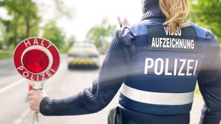 Eine Polizistin, sie eine Schutzweste trägt, hält eine Kelle in der Hand, um Fahrzeuge zu stoppen.