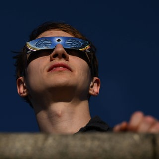 Ein Mann mit Brille schaut die Sonnenfinsternis. In der Mainzer Uniklinik mussten nach der partiellen Sonnenfinsternis zehn Menschen mit Beschwerden behandelt werden. 
